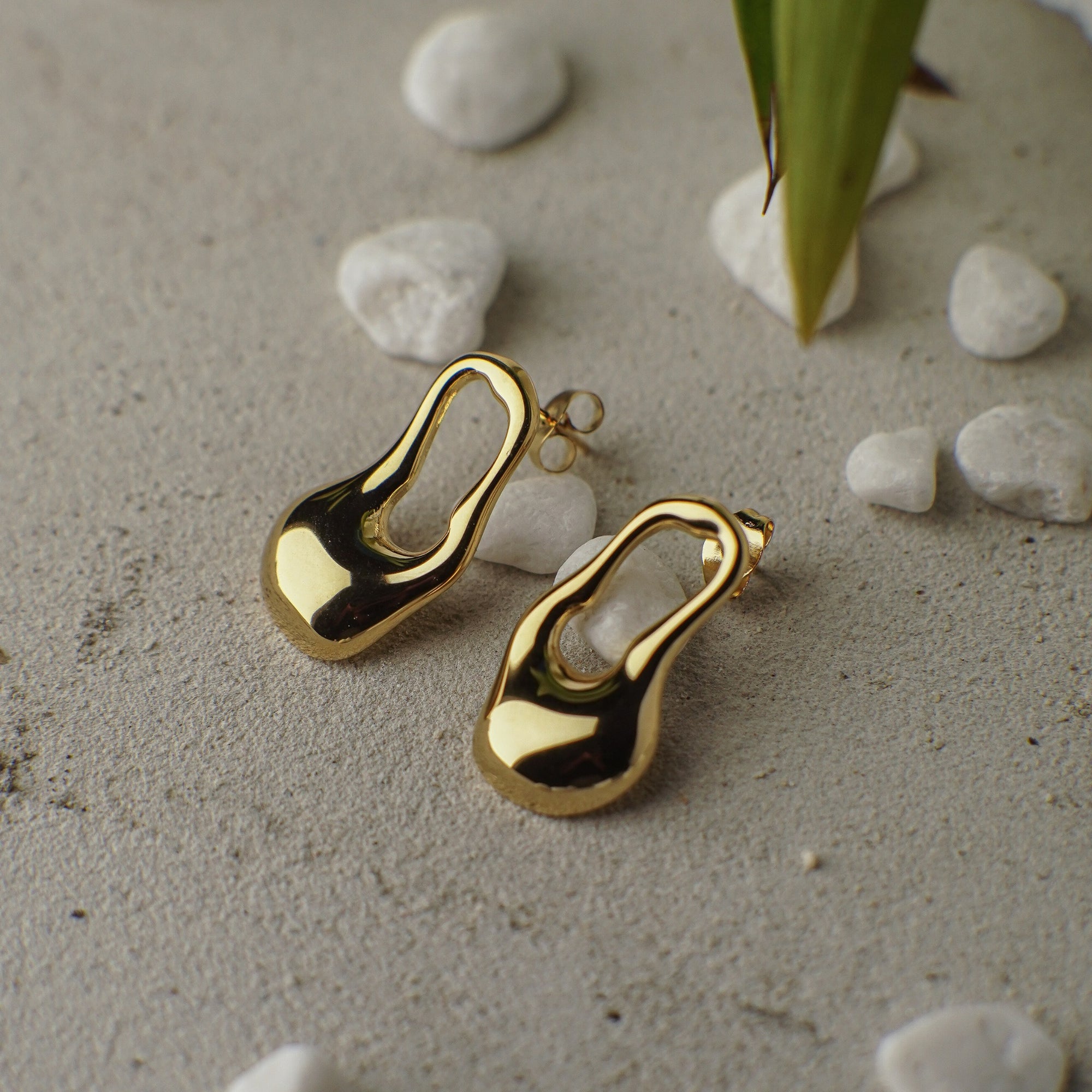 Gold earrings on a textured surface with stones and leaves
