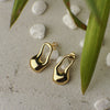 Gold earrings on a textured surface with stones and leaves