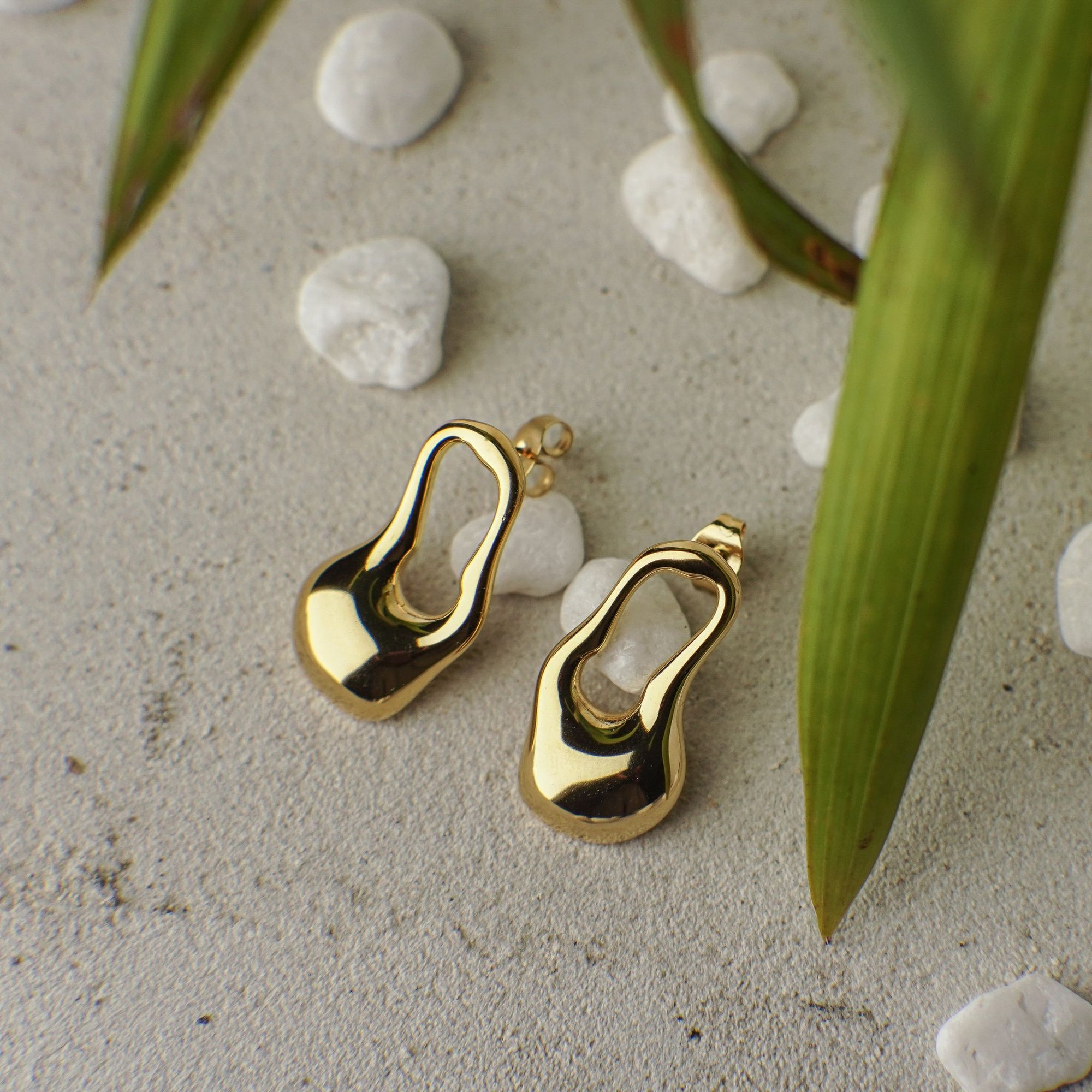 Gold earrings on a textured surface with stones and leaves