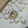 Two interlocking rings, one gold and one silver, on white pebbles.