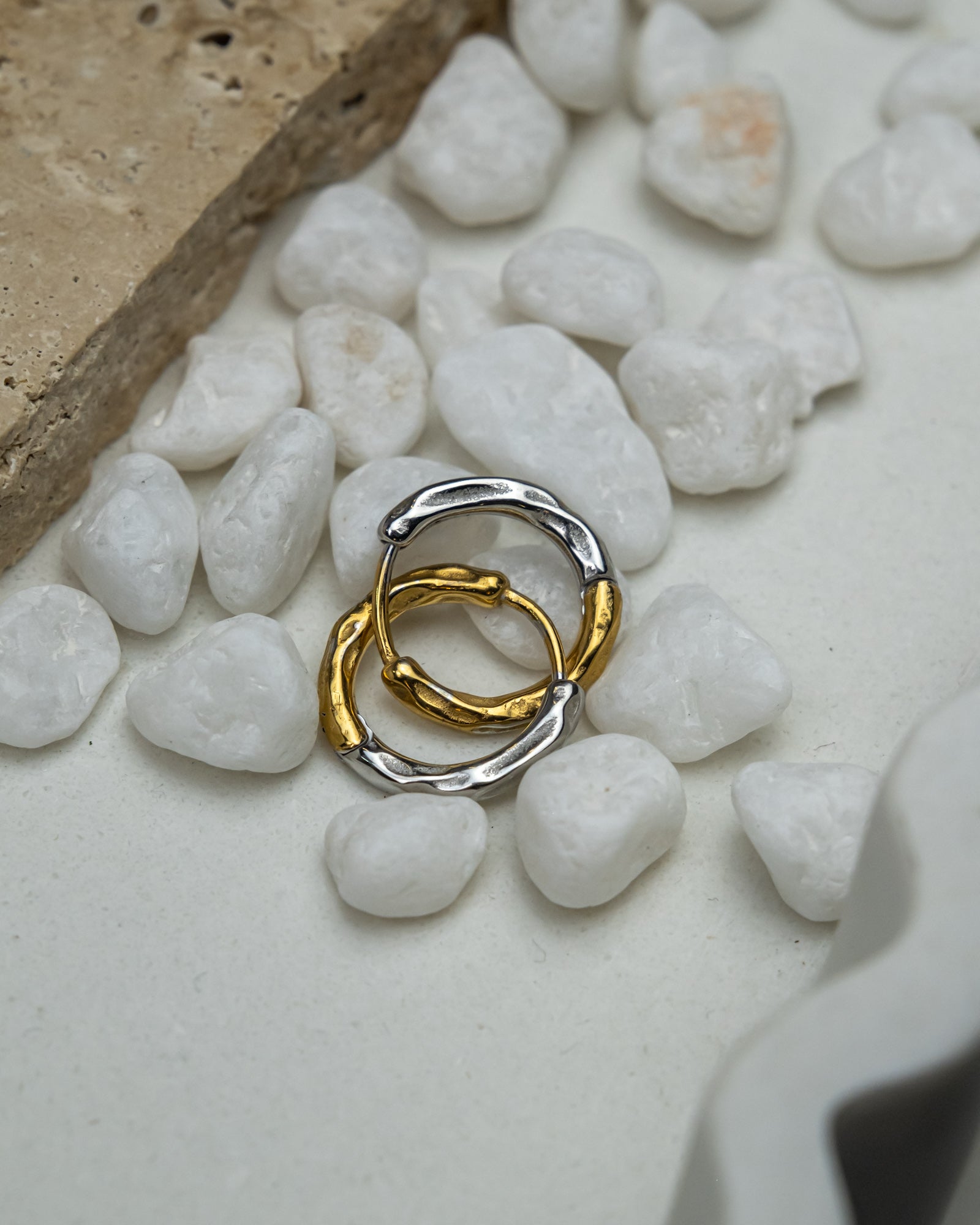Two interlocking rings, one gold and one silver, on white pebbles.
