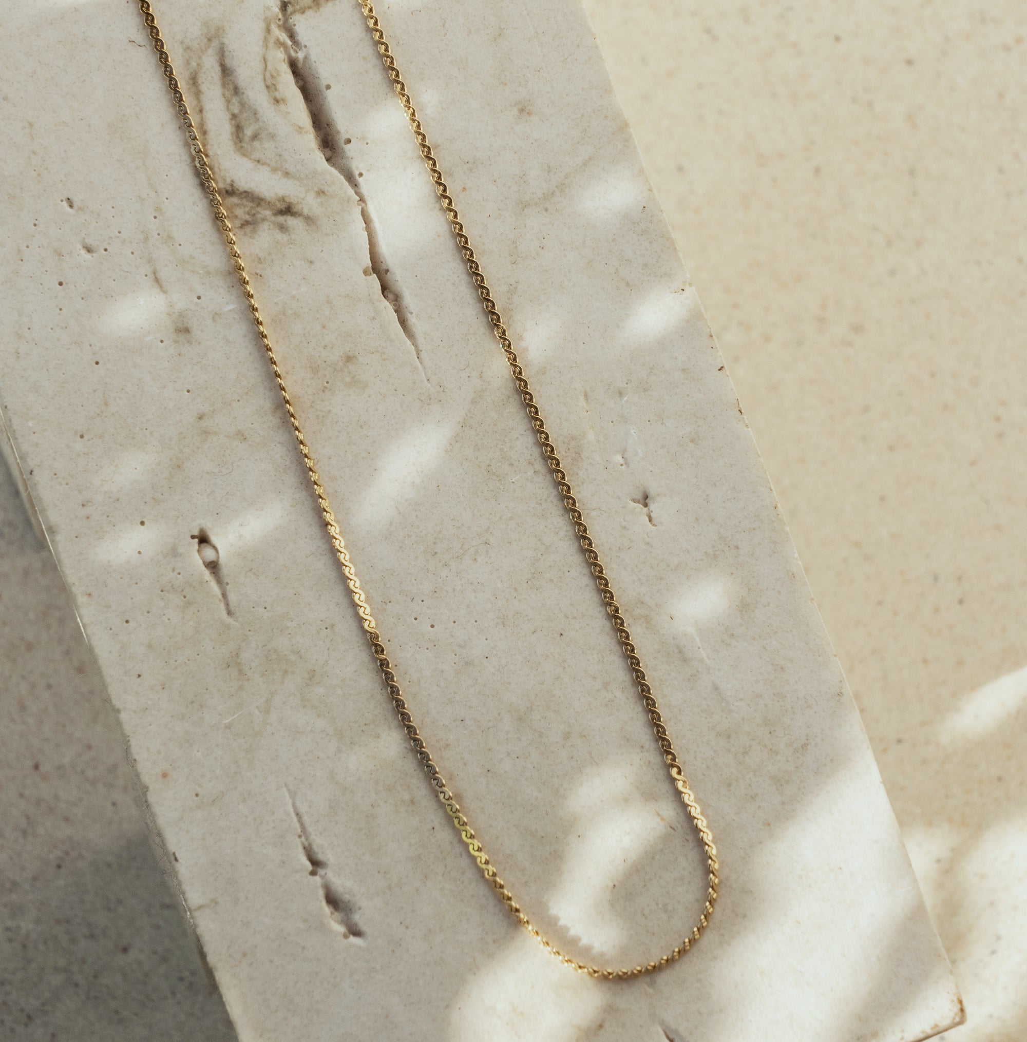 A gold necklace laid out on a flat surface, displaying a twisted chain design.