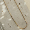 A gold necklace laid out on a flat surface, displaying a twisted chain design.