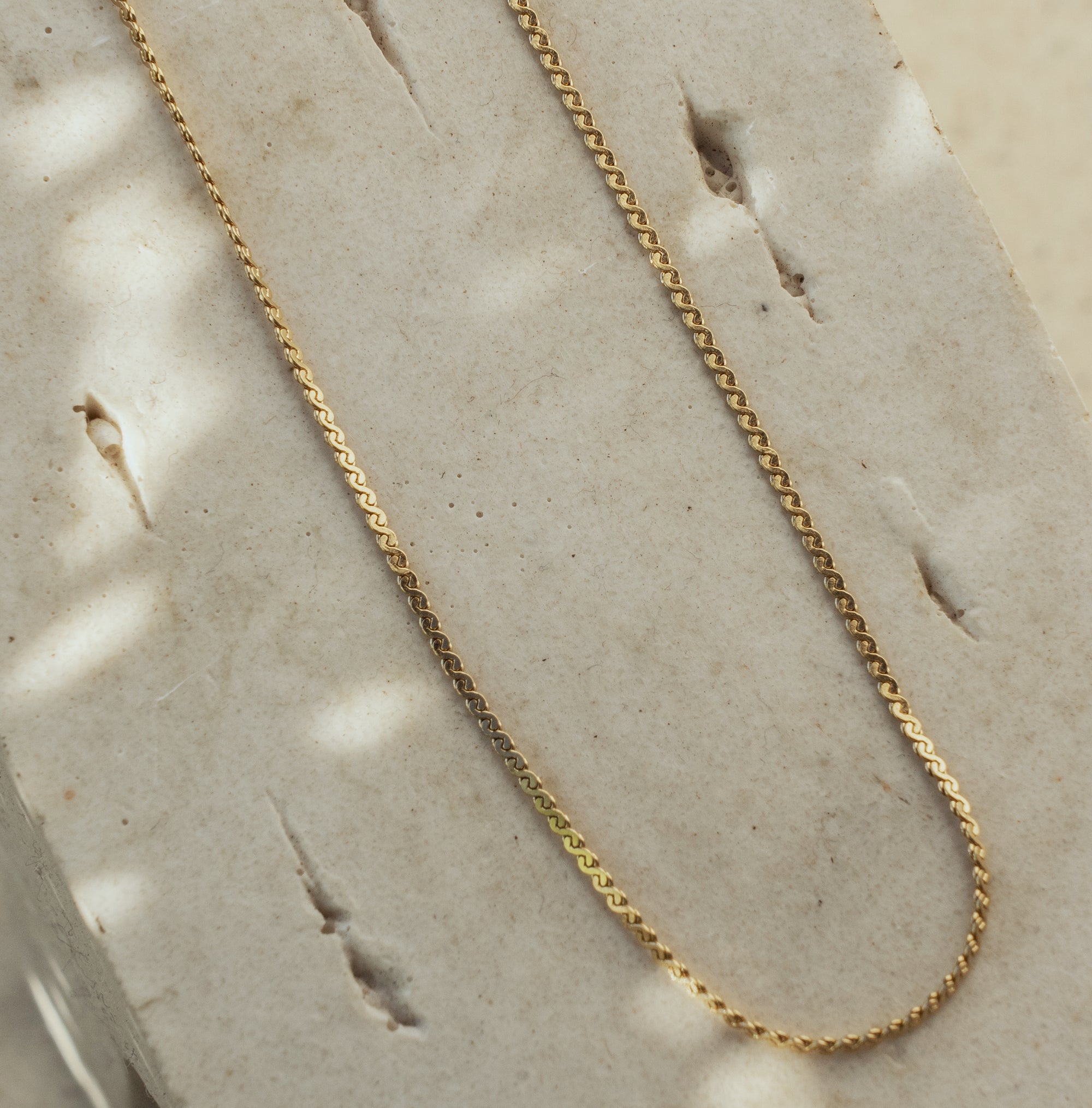 A gold necklace laid out on a flat surface, displaying a twisted chain design.