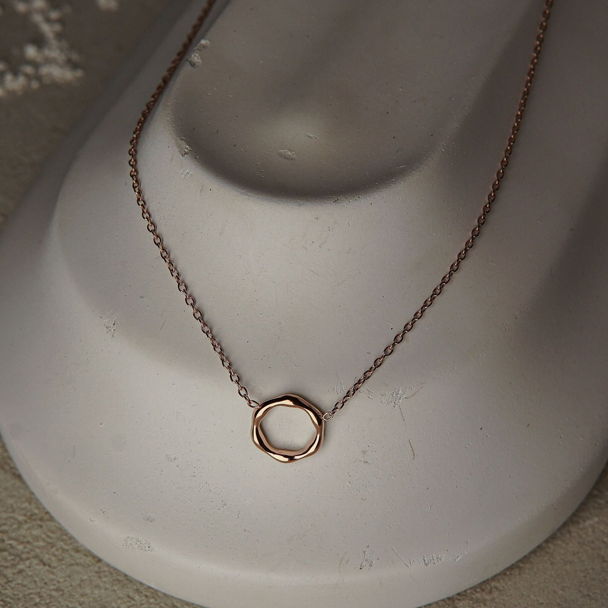 Gold necklace with a circular pendant on a mannequin bust.