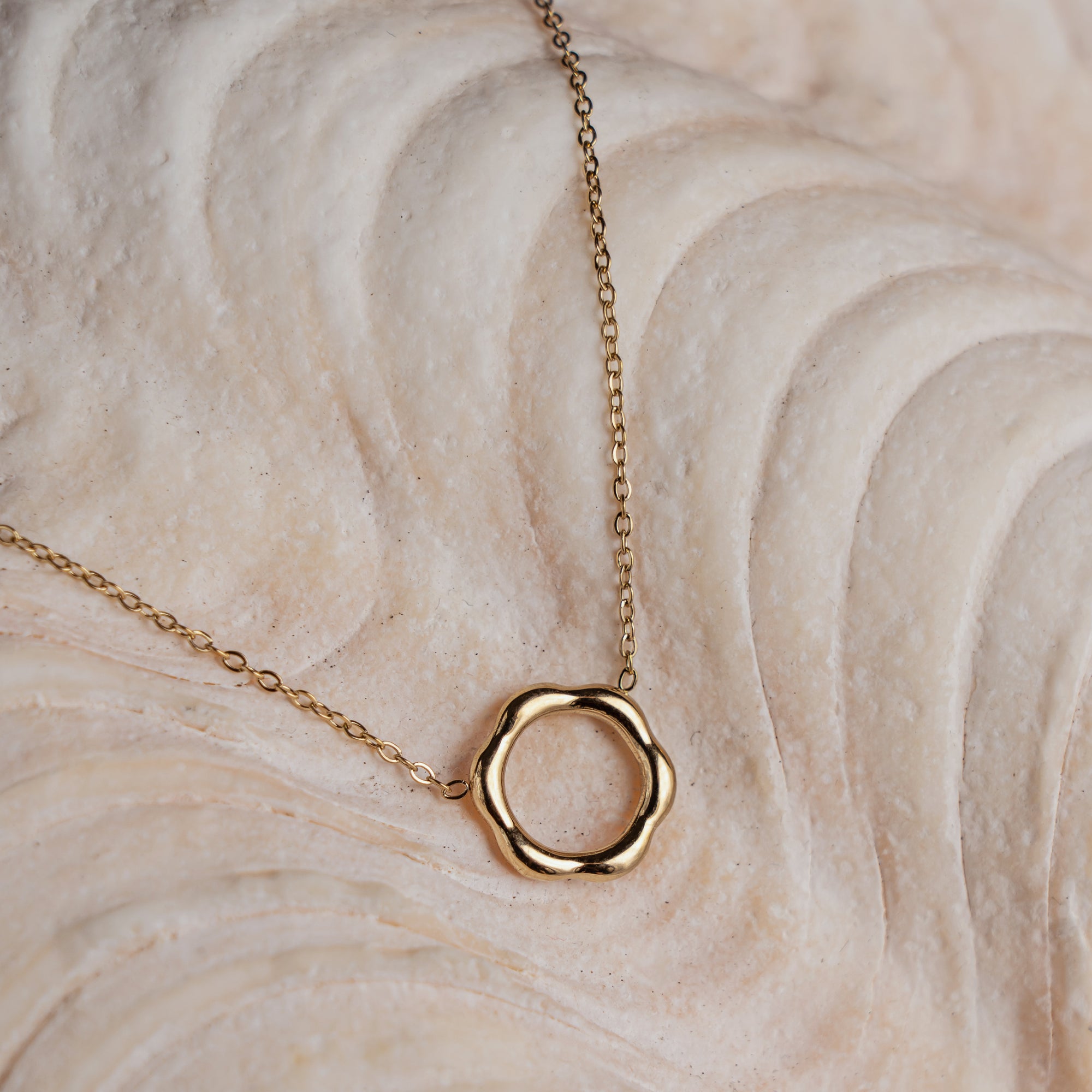 A gold-colored necklace with a rounded hexagon pendant on a textured background.