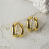 Gold hoop earrings with embedded stones on a textured beige surface