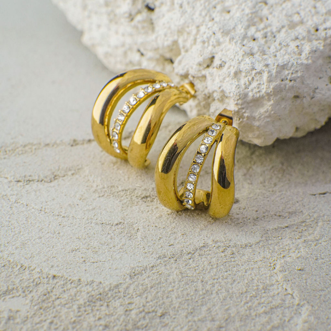 Gold hoop earrings with embedded stones on a textured surface