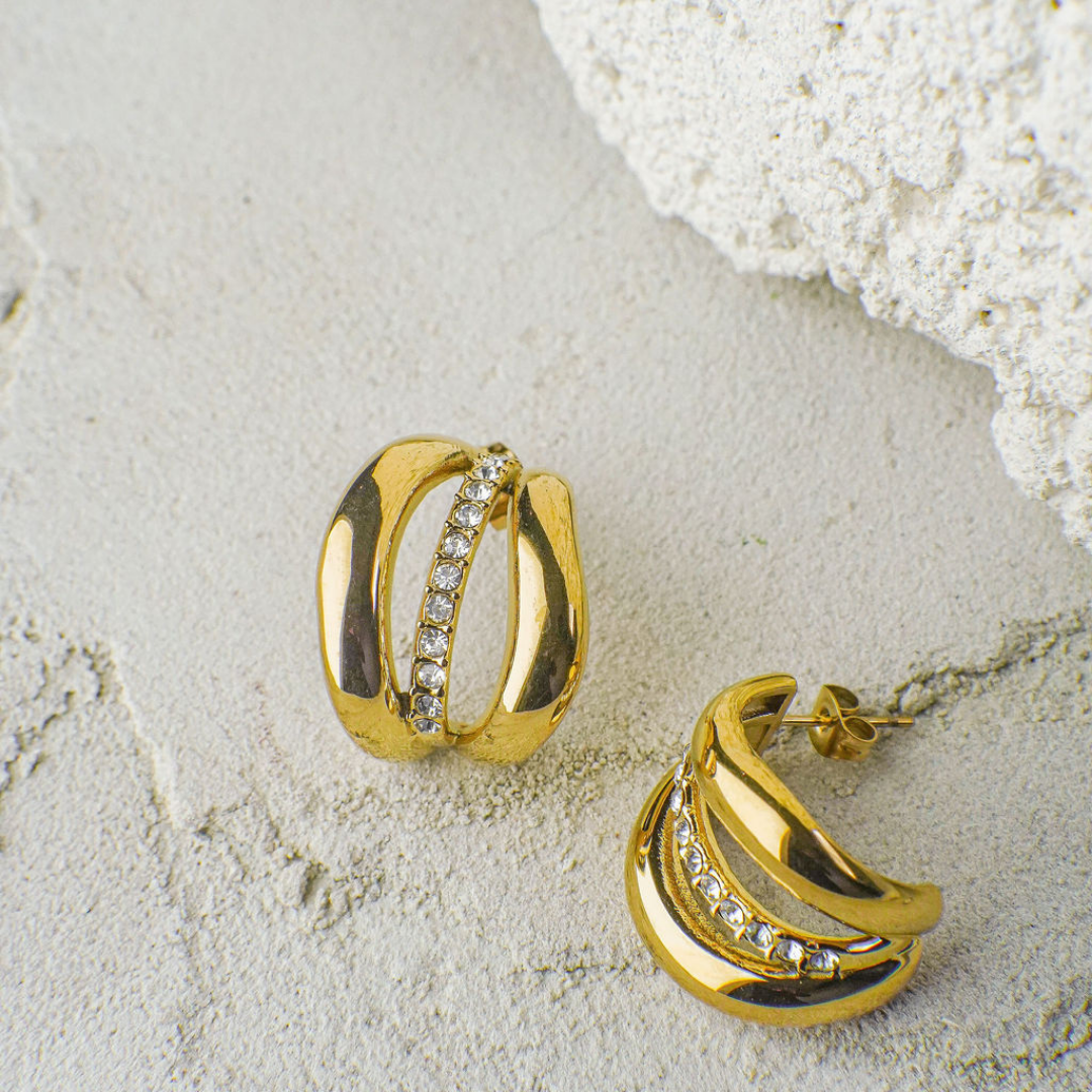 Gold hoop earrings with embedded stones on a textured beige surface