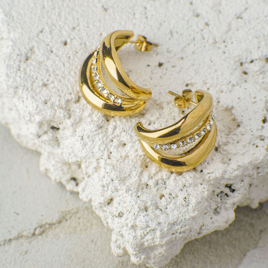Gold hoop earrings with embedded stones on a textured white surface
