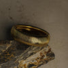 Gold ring with ribbed design on a textured stone surface