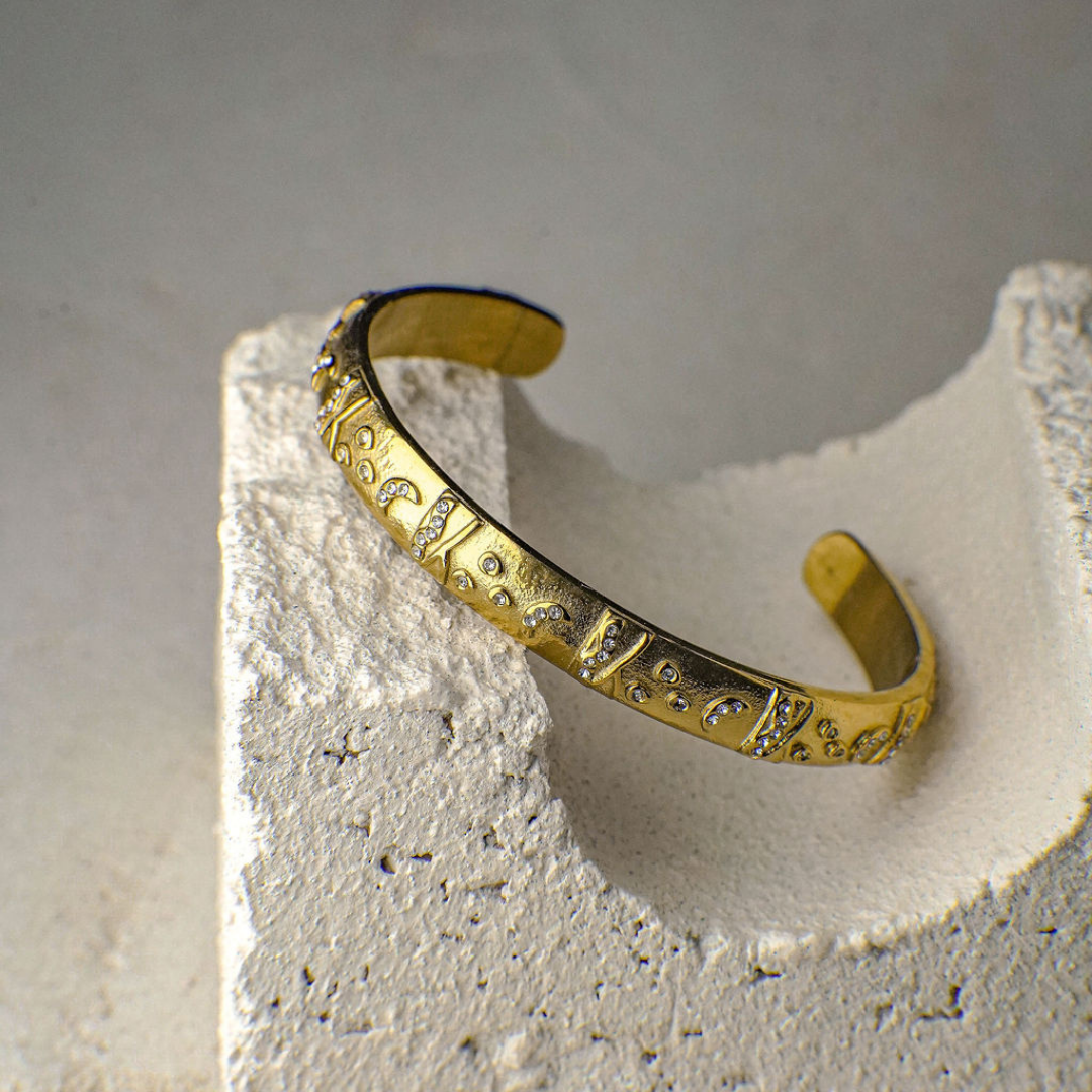 Gold bracelet with intricate designs on a textured stone surface