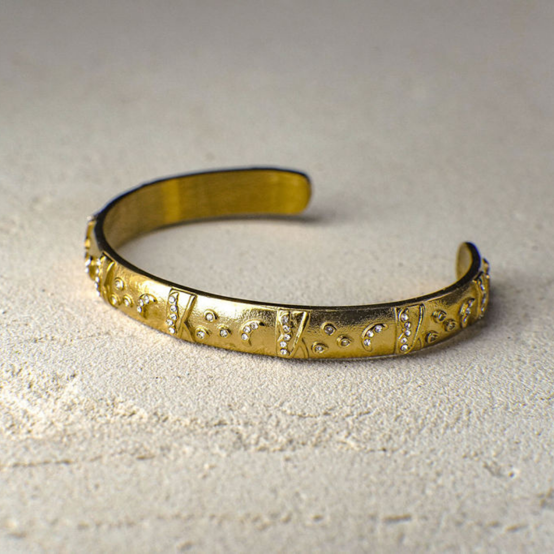 Gold bracelet with decorative patterns on a light gray background