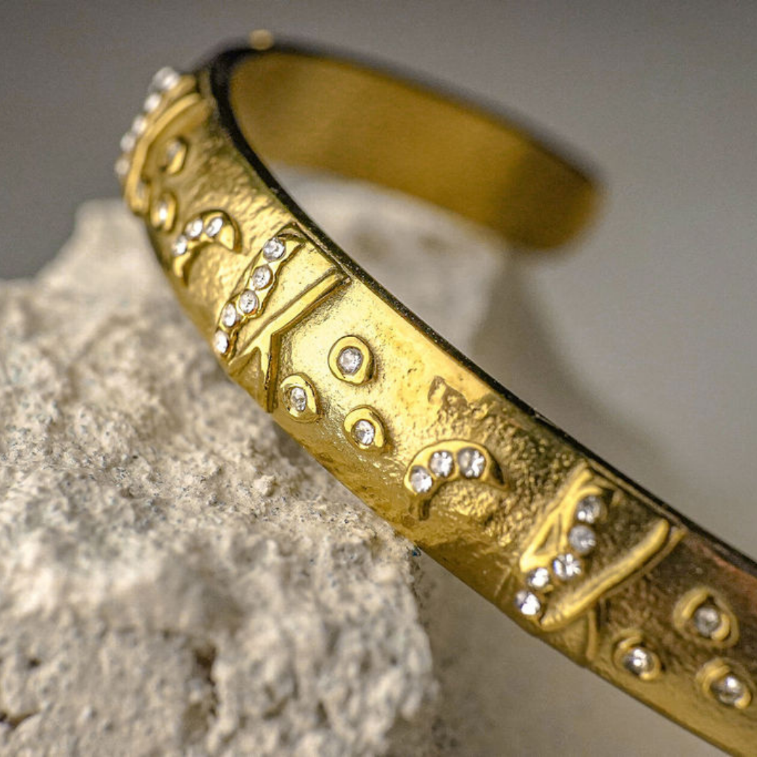 Gold bracelet with intricate designs and small stones on a textured surface