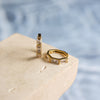 A pair of gold earrings with three crystals on a textured surface