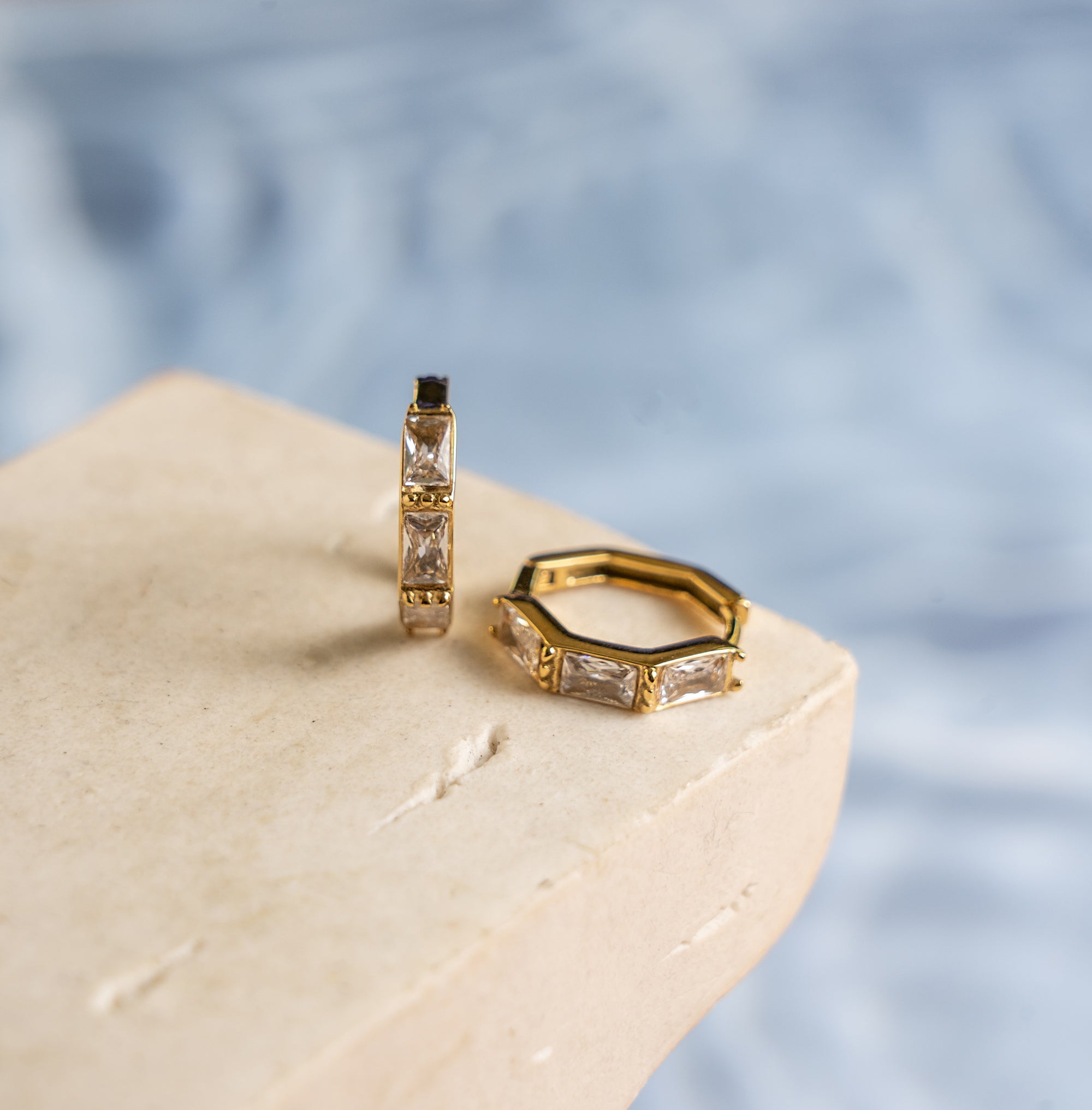 A pair of gold earrings with three crystals on a textured surface