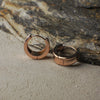 Rose gold hoop earrings on a textured stone surface