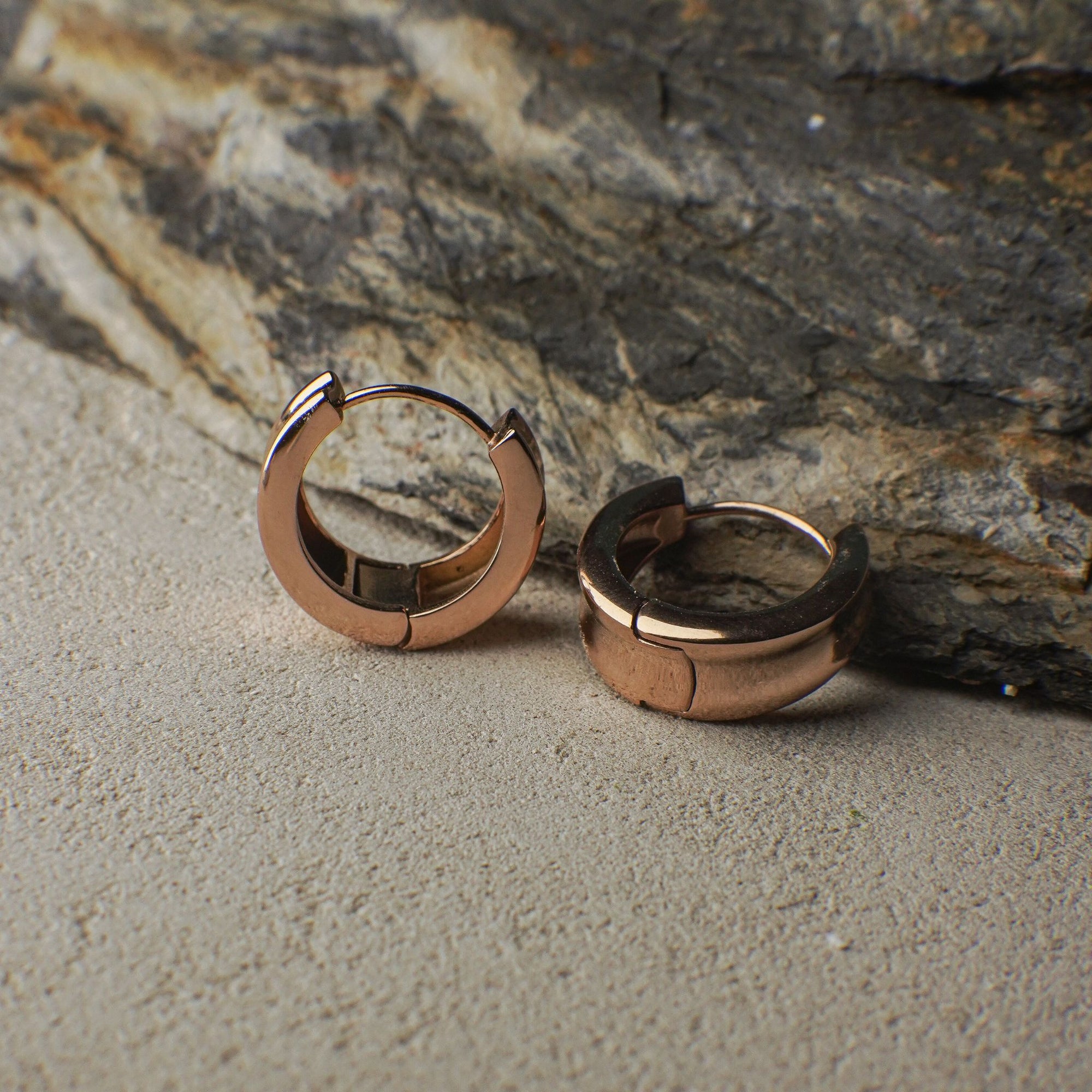 Rose gold hoop earrings on a textured stone surface