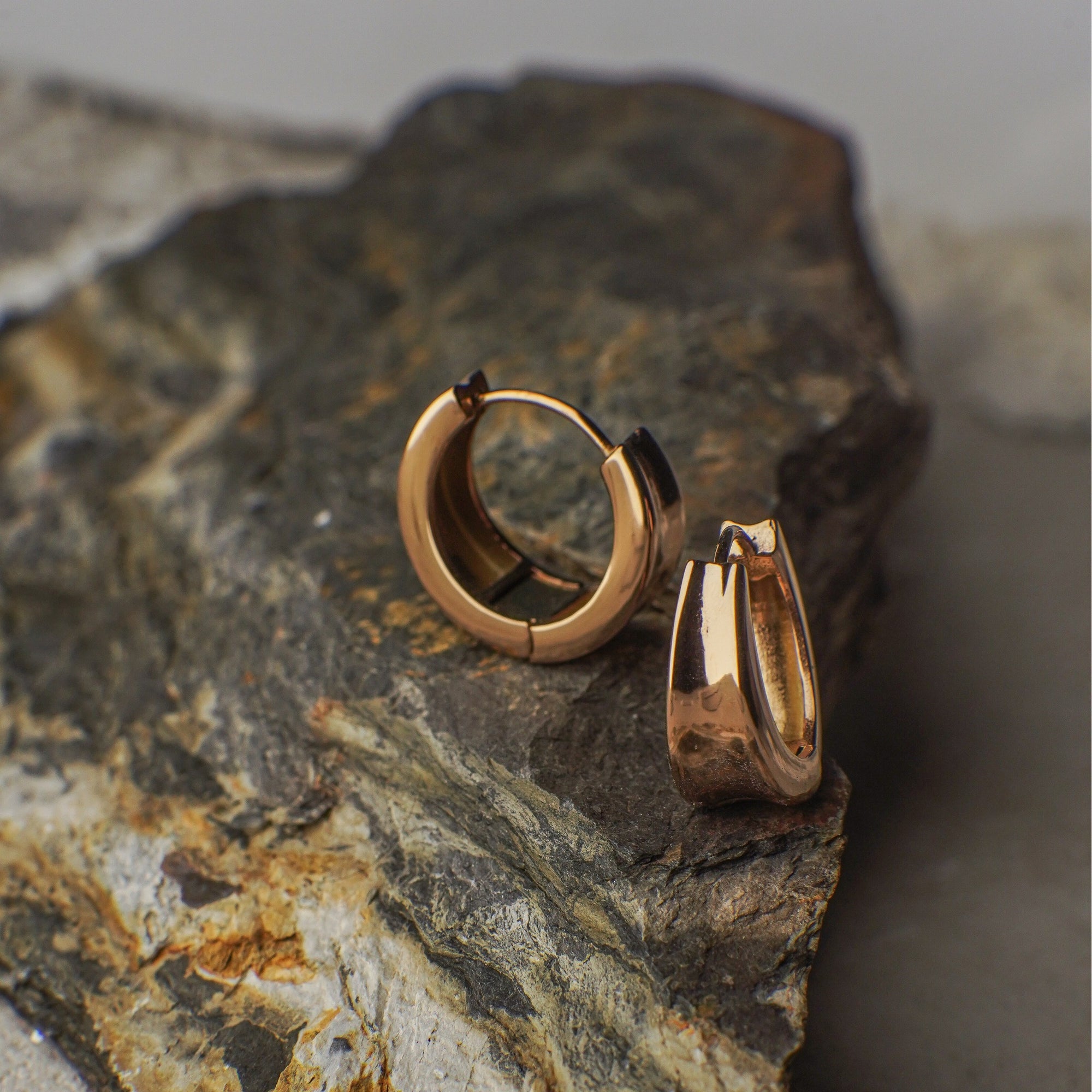Rose gold hoop earrings on a textured stone surface
