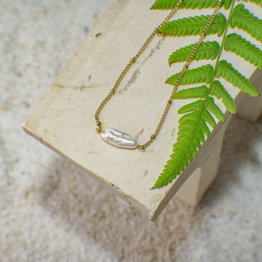 Necklace with a huge pearl pendant on a stone surface with a fern leaf