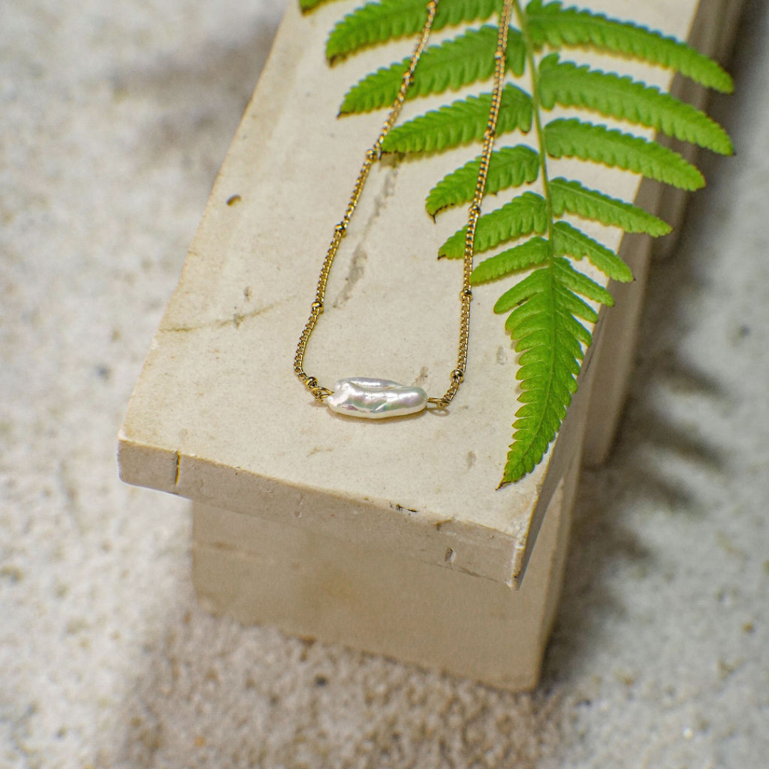 Gold necklace with a pendant on a stone surface with a green leaf