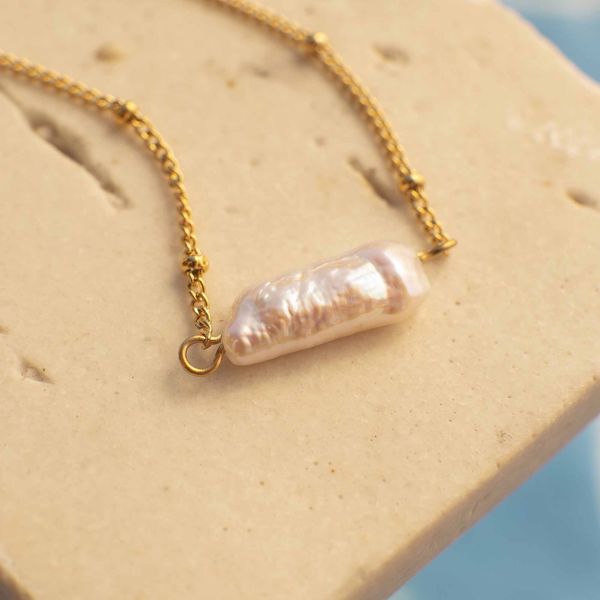 Gold necklace with a large pearl pendant on a textured beige surface