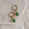 A pair of emerald green drop earrings with gold hoops on a marble surface.