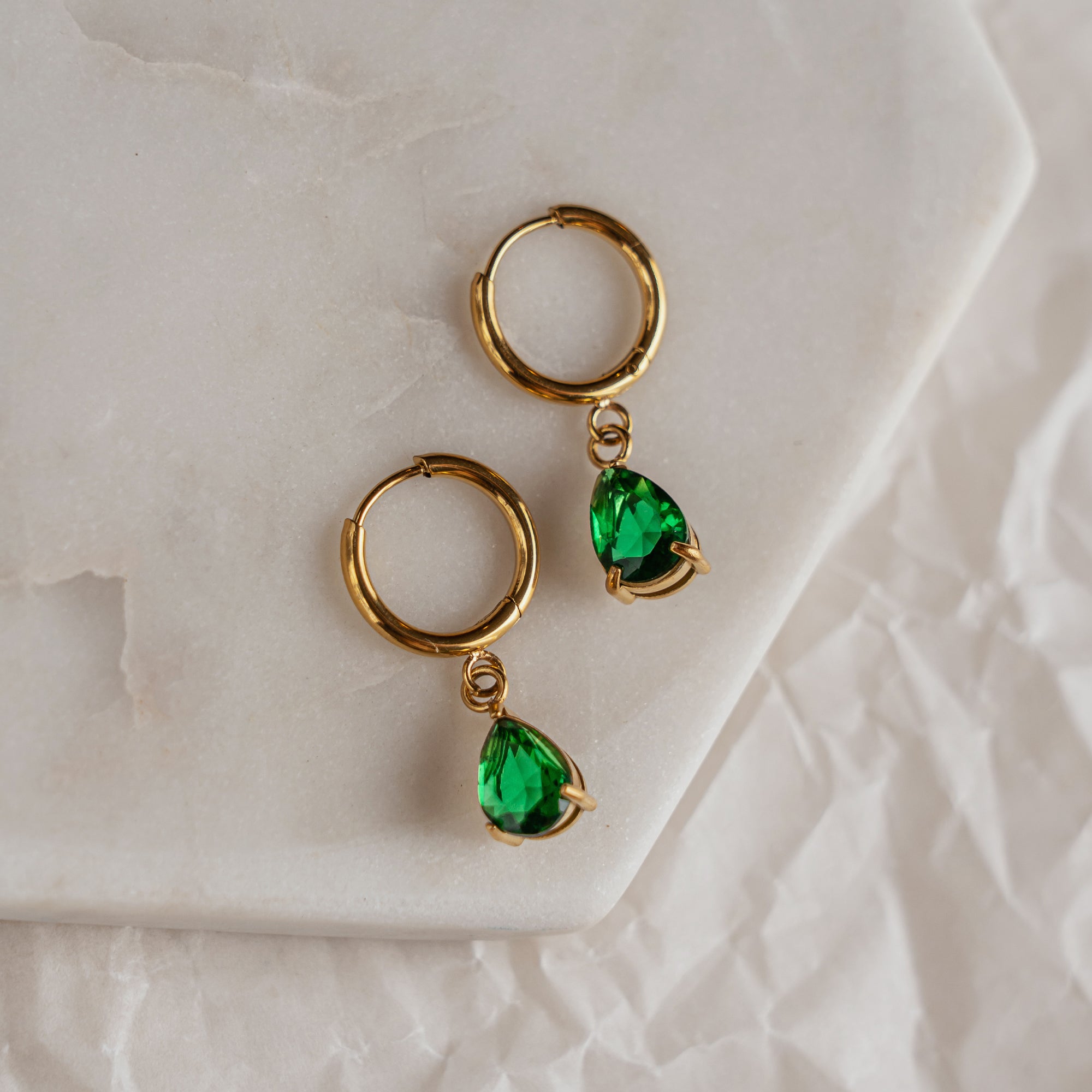 A pair of emerald green drop earrings with gold hoops on a marble surface.