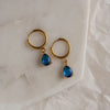 A pair of blue sapphire drop earrings with gold hoops on a marble surface.