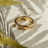 A gold ring with a zirconia center stone, placed on a textured surface with a blurred green background.