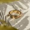 A golden ring with multicolored zirconia stones set in it, placed on a light surface with a blurred green background.