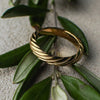 Gold ring with a textured design on green leaves against a neutral background