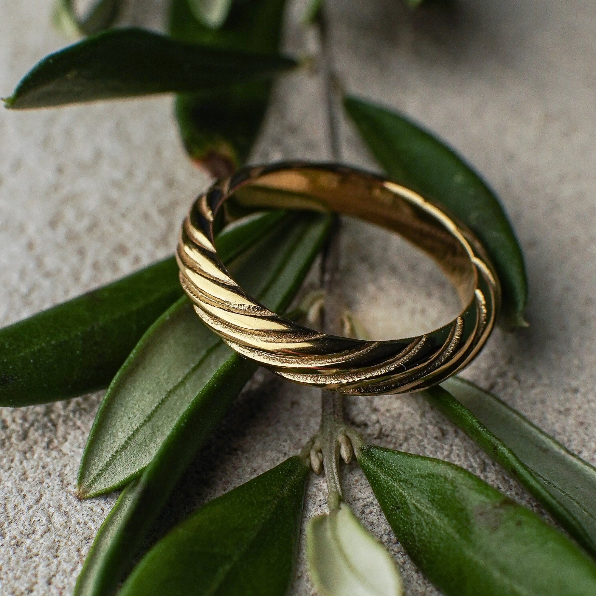 Gold ring with a textured design on green leaves against a neutral background