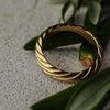 Gold ring with a textured design on a textured surface with green leaves.