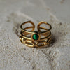 Gold ring with a green gemstone on a sandy surface