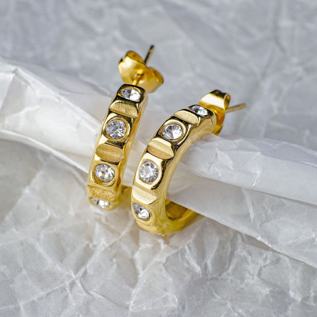 Gold hoop earrings with embedded diamonds on a light gray background