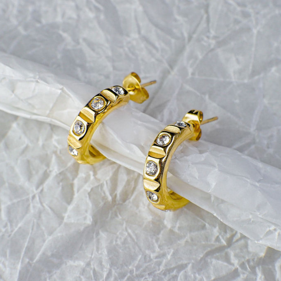 Gold hoop earrings with embedded diamonds on a textured white background