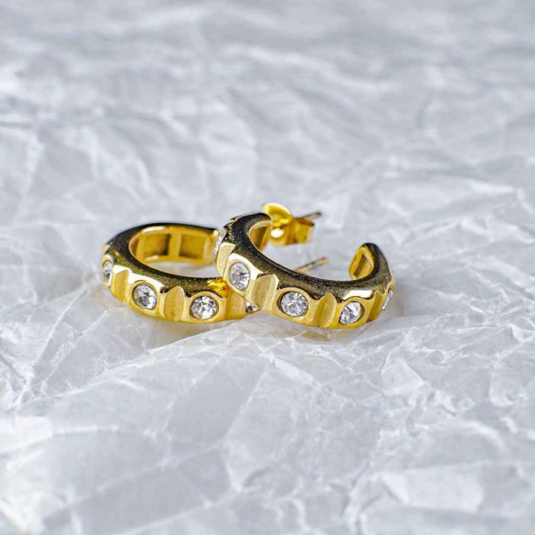 Gold hoop earrings with embedded stones on a textured white background