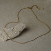 Gold chain necklace draped over a stone on a textured surface