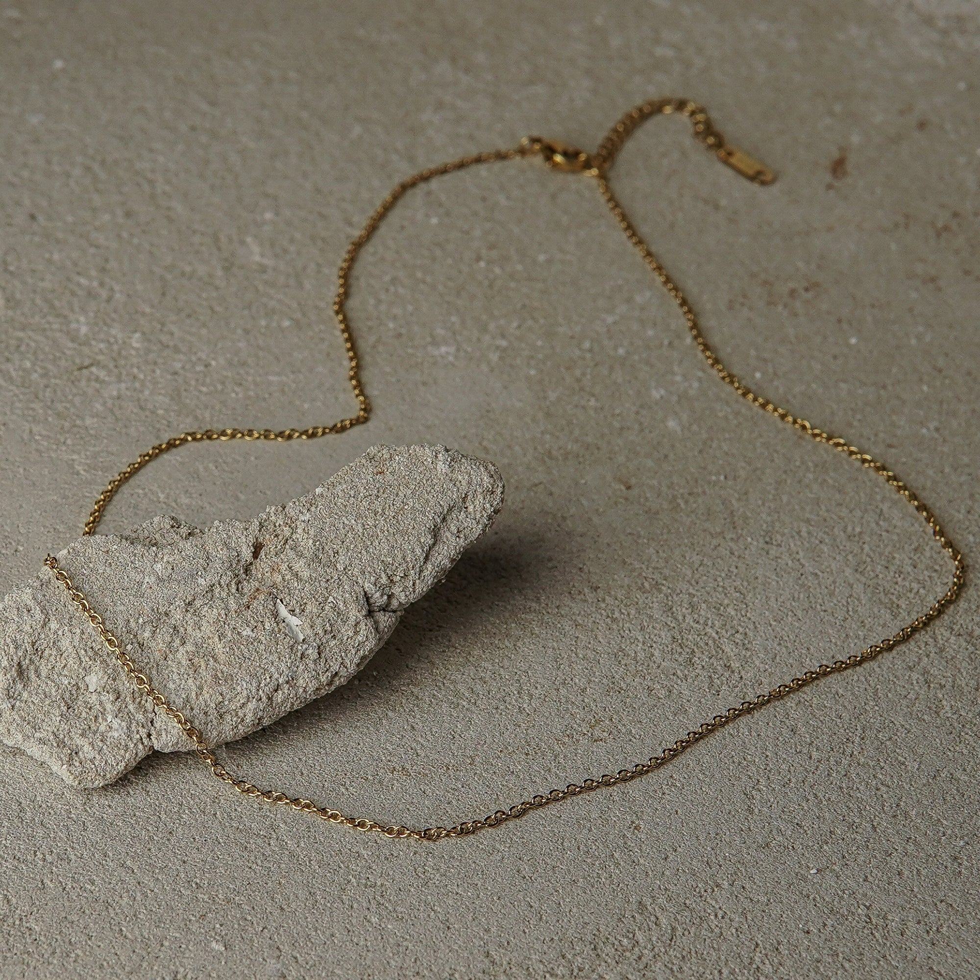 Gold chain necklace draped over a stone on a textured surface