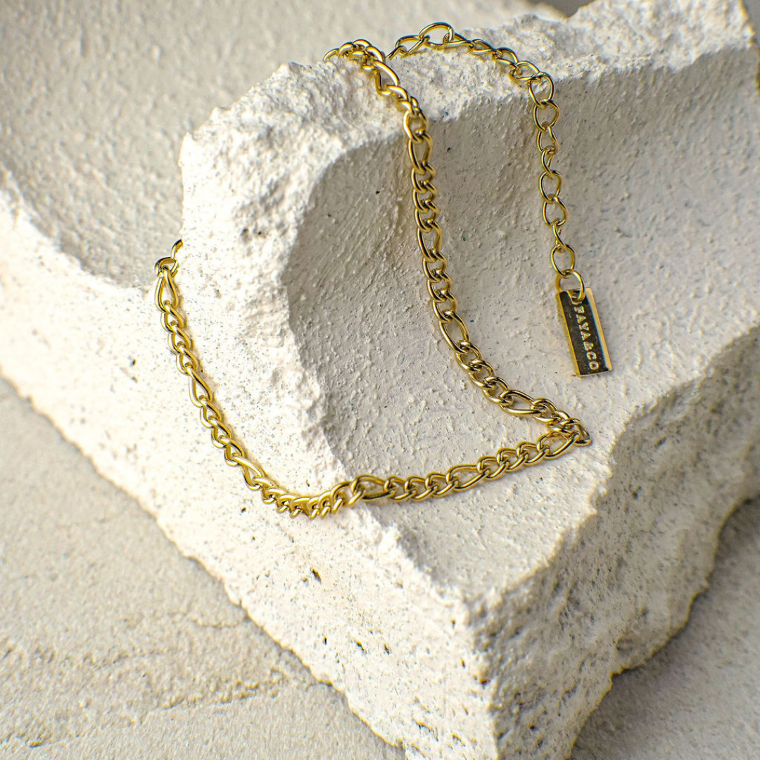 Gold chain bracelet with a tag on a textured stone surface