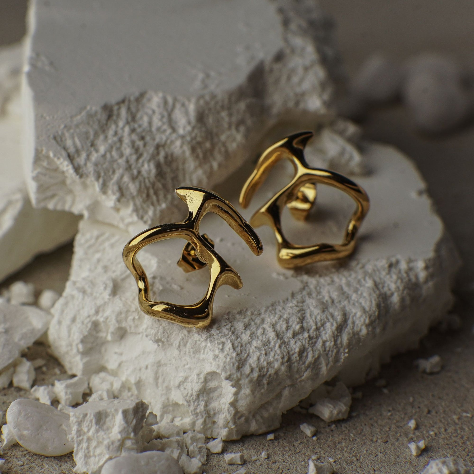 Gold earrings on a textured white surface