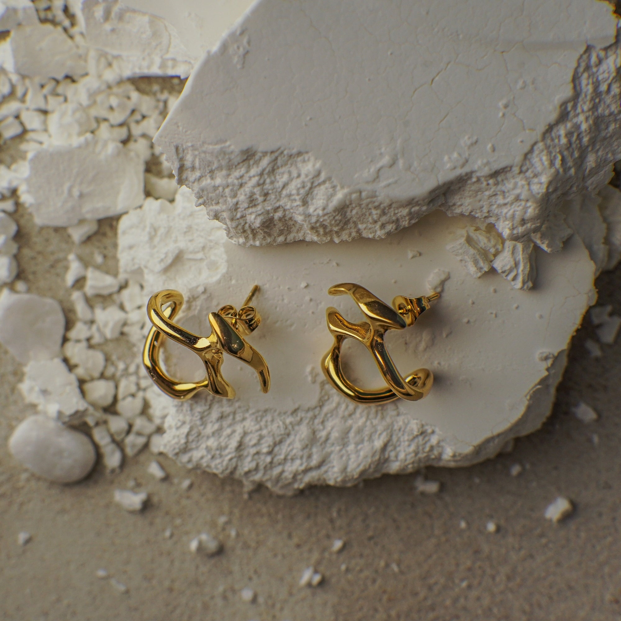Gold anchor-shaped earrings on a textured white surface