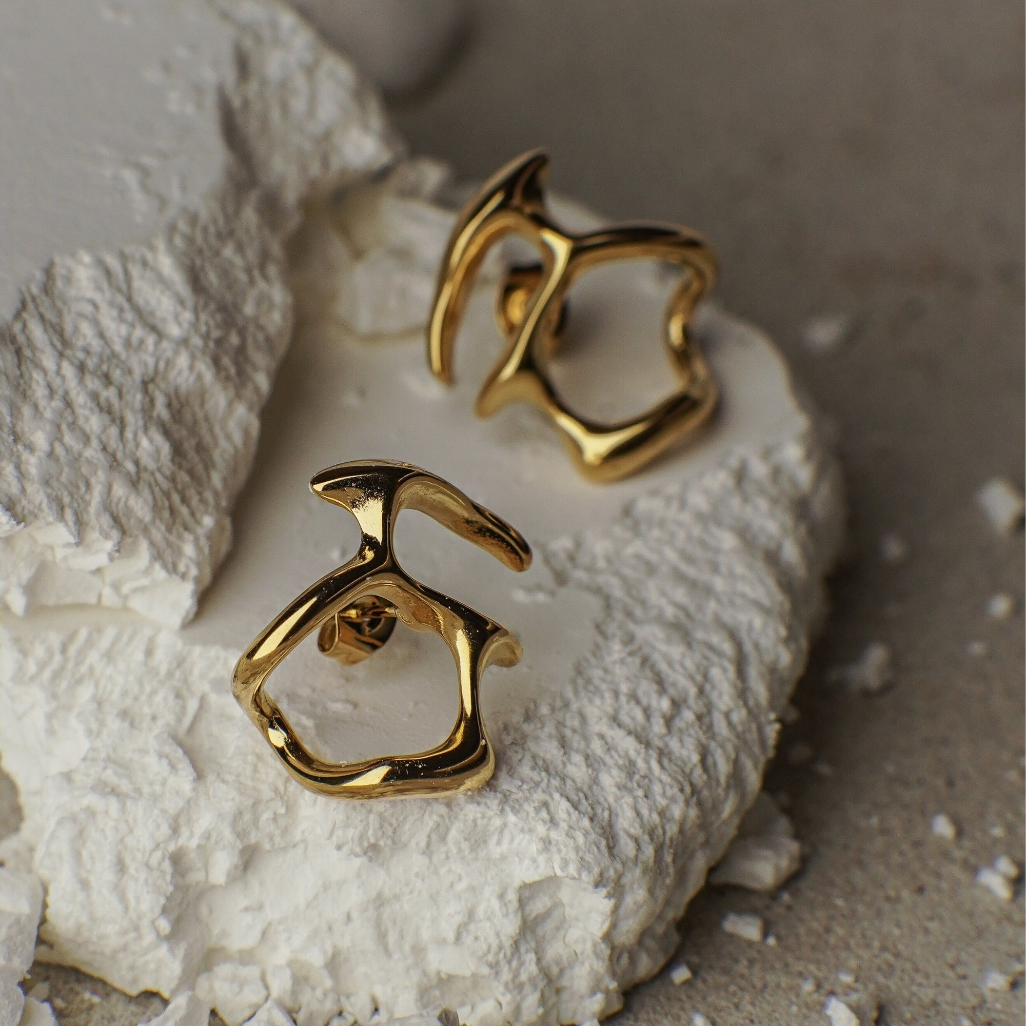 Gold earrings on a textured white surface