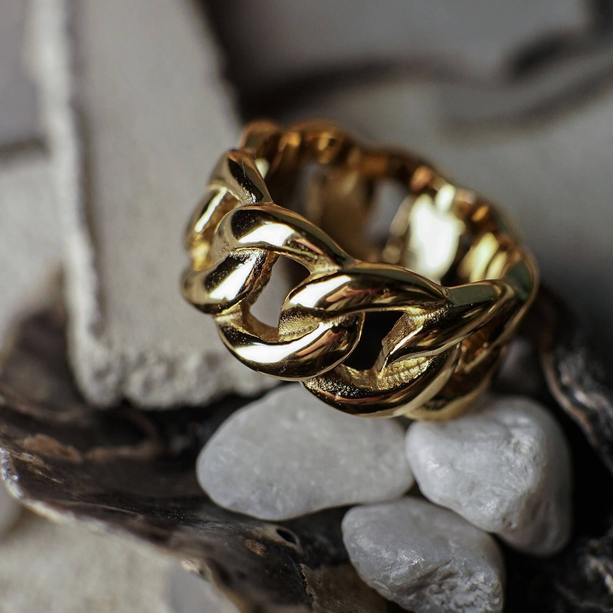 Gold chain-style ring on a textured surface with pebbles