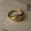 Gold ring with a diamond on a textured beige surface