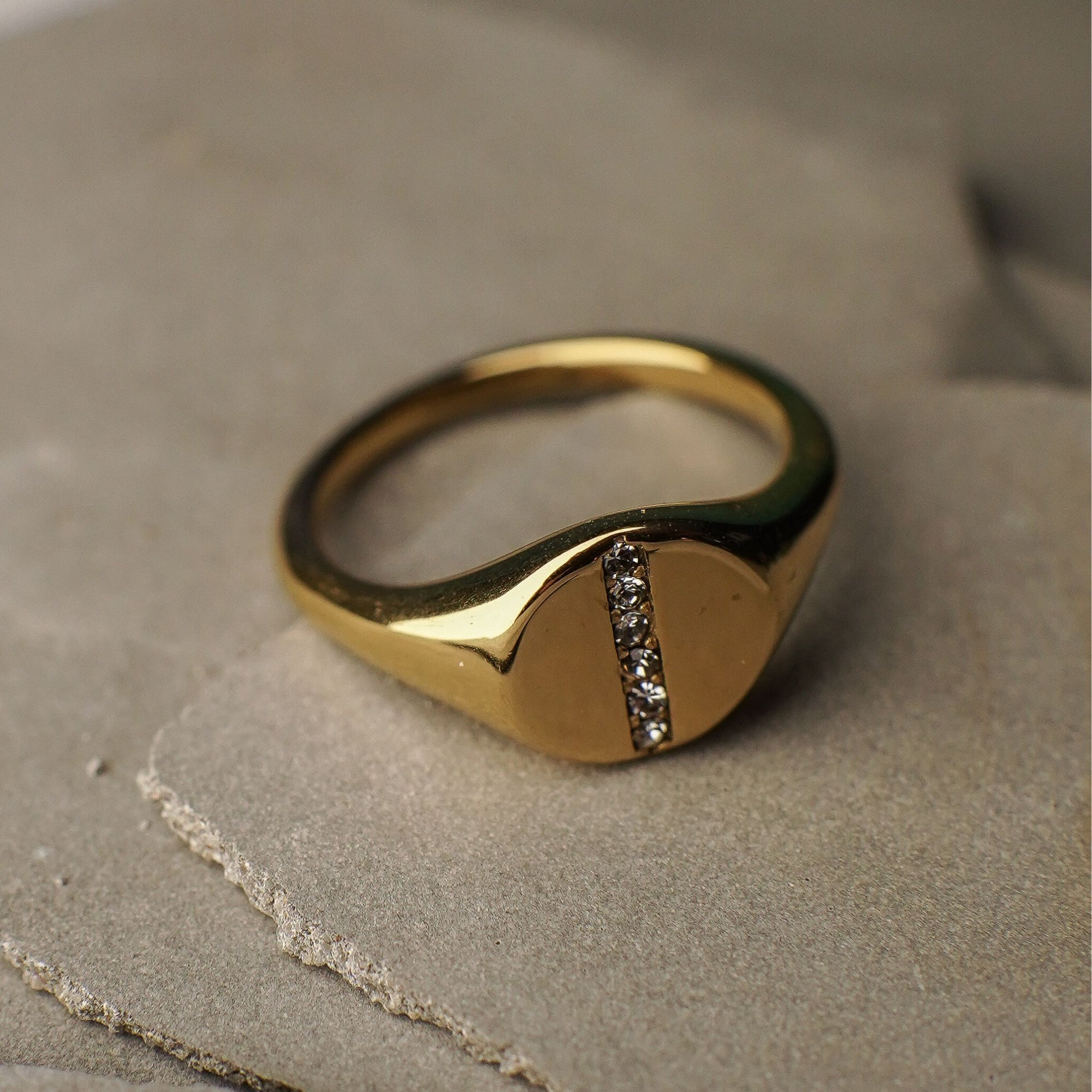 Gold ring with a diamond on a textured beige surface