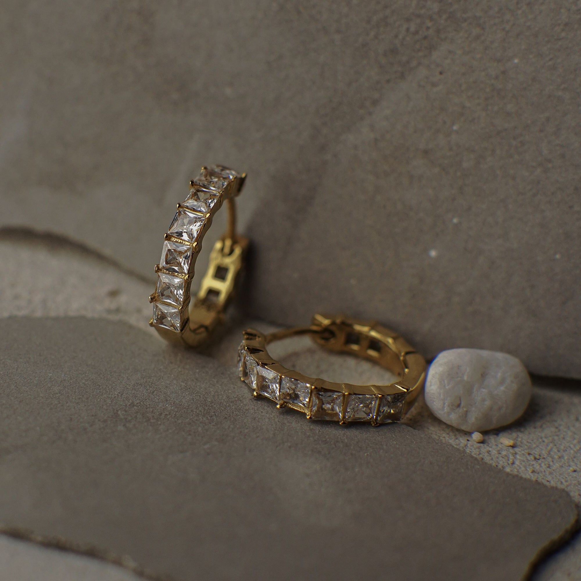 Gold hoop earrings with diamond accents on a textured surface