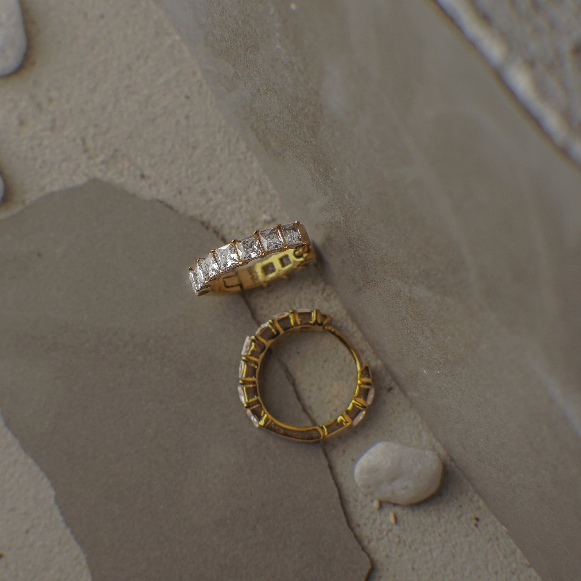 Two gold rings with diamond accents on a textured surface.