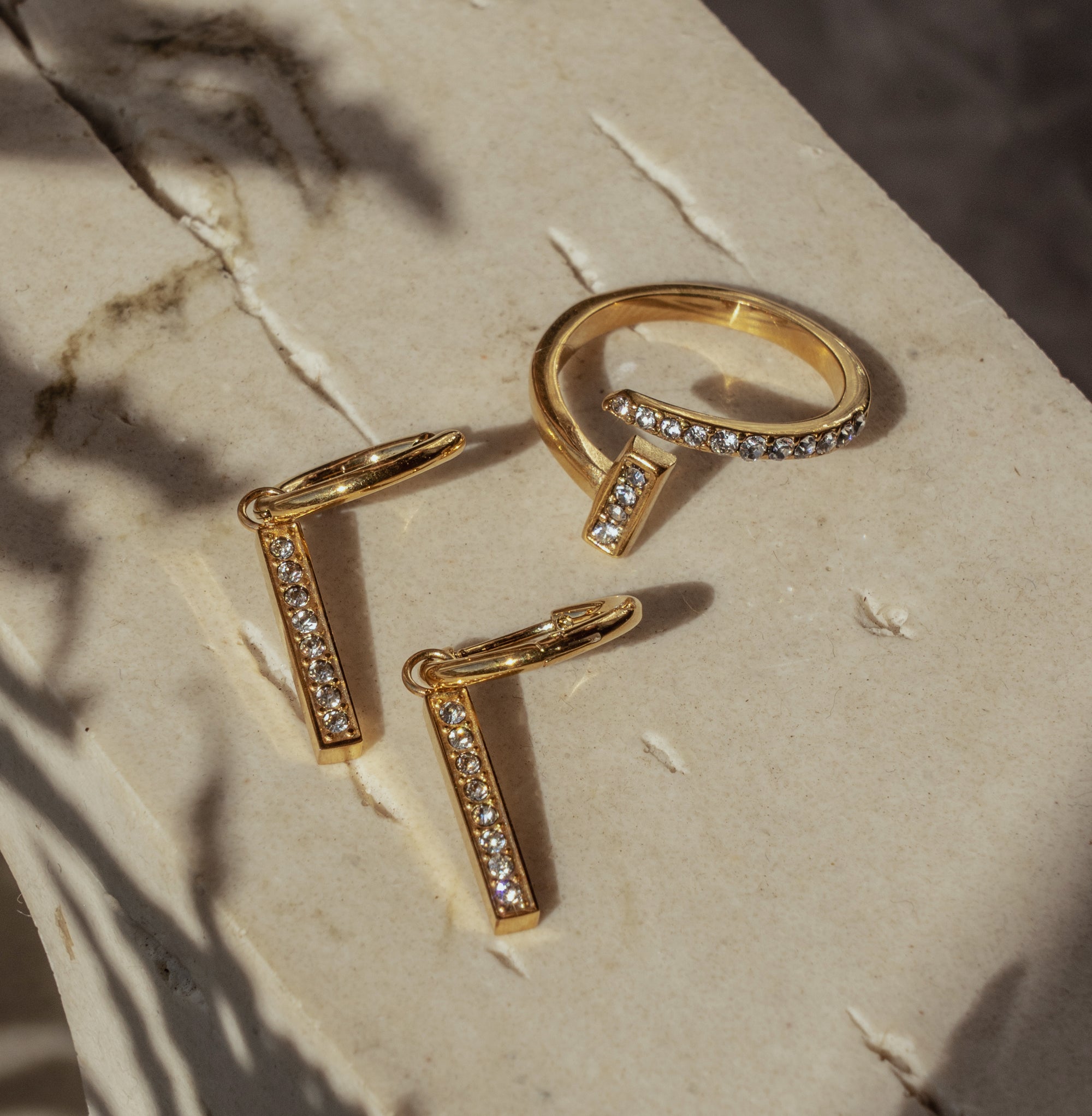 A pair of gold-colored drop earrings with zirconia pendants, displayed on a marble surface.